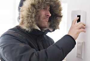 Man wearing a black parka adjusting the inside thermostat.