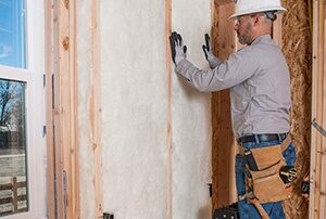Worker installing batt insulation in a wall.