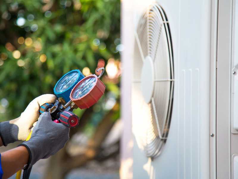 Hands holding a testing device near an HVAC system outside.