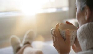 Woman enjoying a warm drink indoors on a sunny winter morning.
