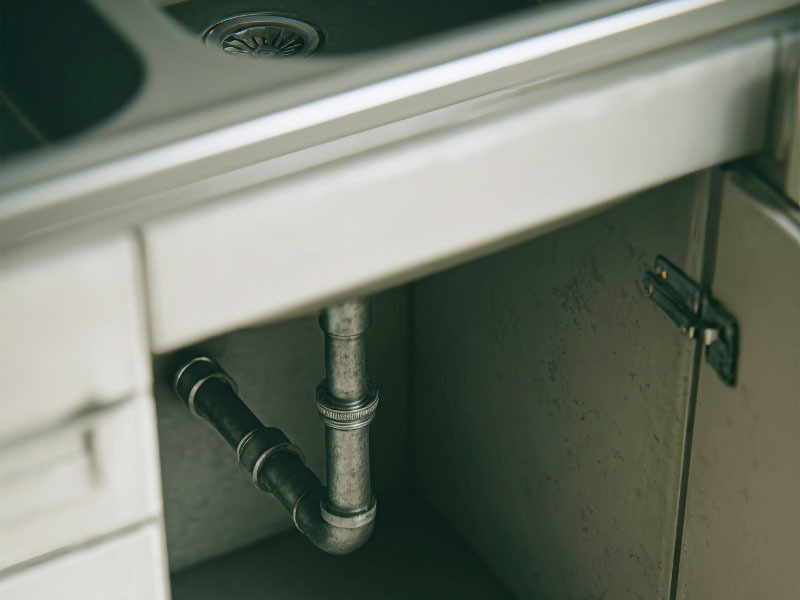 Under-sink plumbing setup with metallic pipes and empty cabinet space in modern kitchen decor