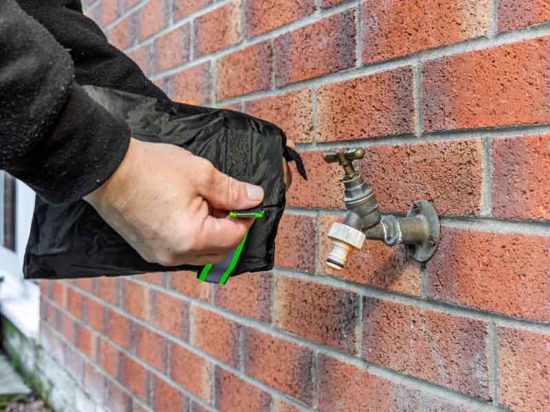 Person Installing Winter Frost Protection Insulated Tap Cover on Brass Garden Brick Wall Water Faucet.