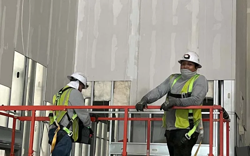 Two Hayes Insulation professionals in safety gear on a scissor lift installing fiberglass insulation into the wall girts of a commercial metal building in Nashville.