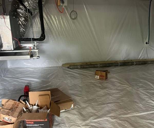 Boxes of specialized sealing materials and TYPAR construction supplies sit on a freshly installed white vapor barrier during a crawl space encapsulation project by Hayes Insulation.