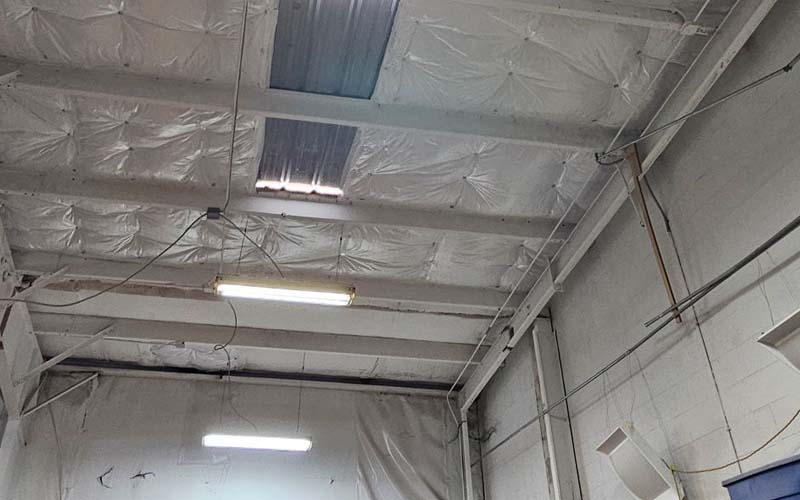 Finished installation of white vinyl-faced fiberglass insulation in a commercial metal building ceiling.