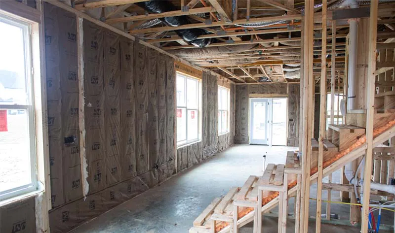 Kraft-faced fiberglass batt insulation installed in framed exterior walls of a new construction home with exposed ceiling joists and ductwork.