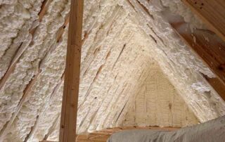 Spray foam insulation applied between roof rafters. Spray foam insulation applied between roof rafters in a peaked attic with HVAC ductwork visible below.