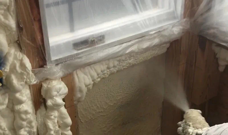 Spray foam insulation applied around a window rough opening and framed wall cavity during new construction.