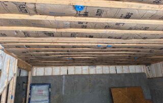 Kraft-faced fiberglass batt insulation along basement ceiling joists above framed walls and a concrete foundation.
