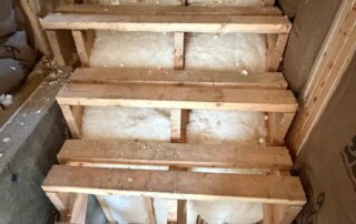 Fiberglass batt insulation installed in the wall framing behind open basement stair treads.