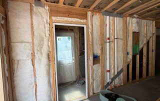 Unfaced fiberglass batt insulation in framed basement walls around an exterior doorway, with kraft-faced batts in the ceiling joists.